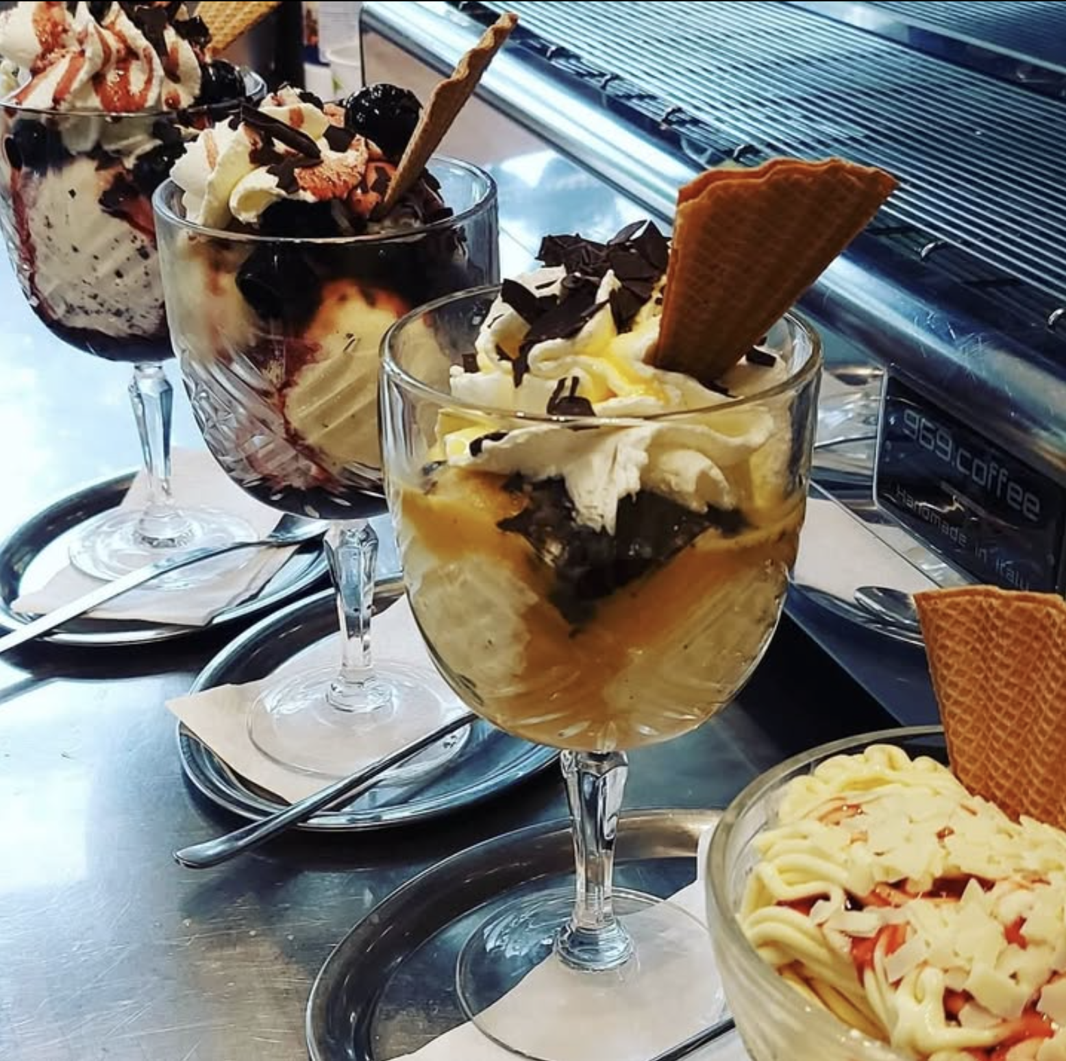 Eisbecher mit Sahne, Schokolade und Waffel auf der Theke, daneben ein Spaghettieis