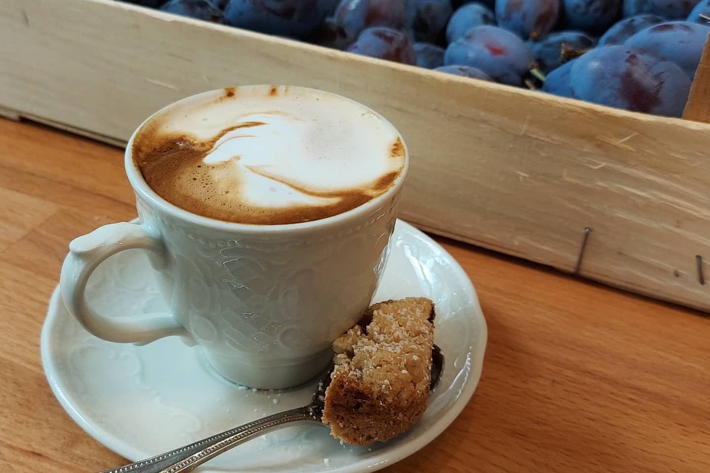 Cappuccino mit Milchschaum, dahinter eine Kiste frischer Zwetschgen